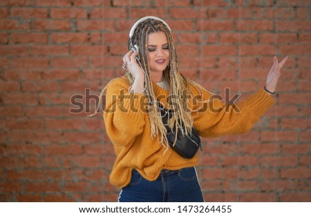 Happy young woman with headphones. Brick wall