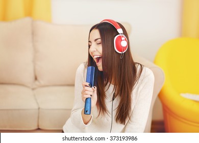 Happy Young Woman With Headphones And Comb Singing At Home