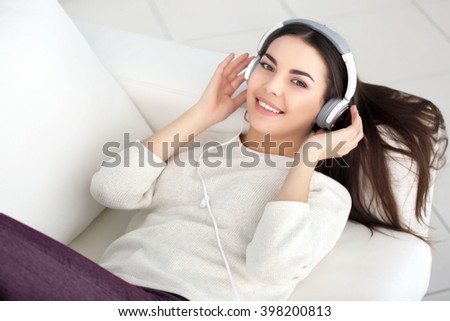Happy young woman with headphones listening to music on a sofa at home