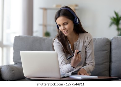 Happy young woman in headphones speaking looking at laptop making notes, girl student talking by video conference call, female teacher trainer tutoring by webcam, online training, e-coaching concept - Shutterstock ID 1297544911