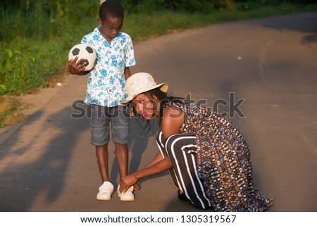 happy young woman helping her son to put on sneakers on the road.Sitting standing while holding a soccer ball