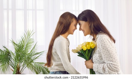 Happy Young Woman And Her Child Celebrating Mother's Day Together. Beautiful Little Daughter And Her Mom Holding Fresh Flowers In Her Hands Looking At Each Other And Smiling. Profile View. Banner