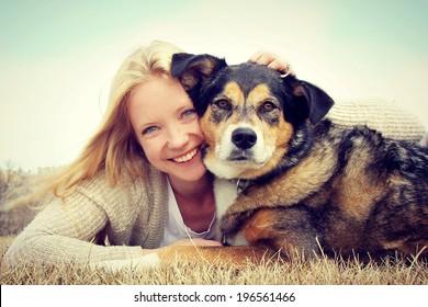 A Happy Young Woman And Her German Shepherd Dog Are Laying On The Grass Outside Hugging. Vintage Style Color.