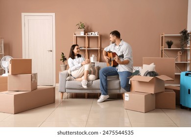 Happy young woman with her husband playing guitar in room on moving day - Powered by Shutterstock