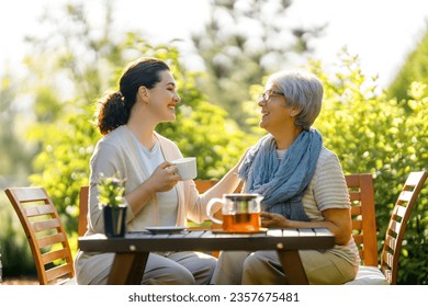 Happy young woman and her mother drinking tea in summer morning. Family sitting in the garden with cups and enjoying the conversation. - Powered by Shutterstock