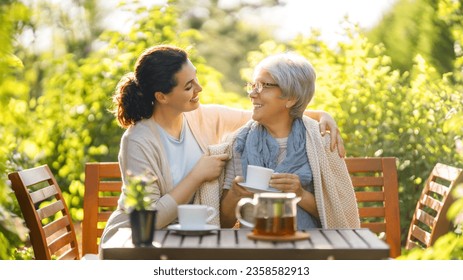 Happy young woman and her mother drinking tea in summer morning. Family sitting in the garden with cups and enjoying the conversation. - Powered by Shutterstock