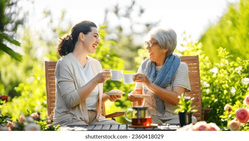 Happy young woman and her mother drinking tea in summer morning. Family sitting in the garden with cups and enjoying the conversation. - Powered by Shutterstock