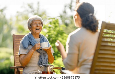 Happy young woman and her mother drinking tea in summer morning. Family sitting in the garden with cups and enjoying the conversation. - Powered by Shutterstock