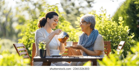 Una joven feliz y su madre tomando té en la mañana de verano. Familia sentada en el jardín con tazas y disfrutando de la conversación.