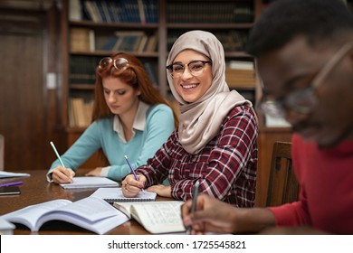 Happy young woman in hijab at university library looking at camera. Portrait of smiling female student wearing abaya and spectacles feeling confident. Islamic girl studying with multiethnic students. - Powered by Shutterstock