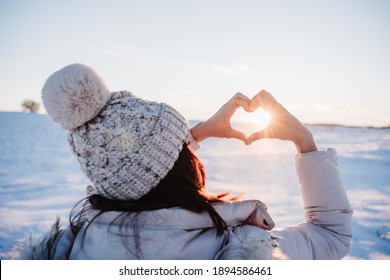 Happy Young Woman Hiking In Snowy Mountain At Sunset Doing A Heart Shape With Hands. Winter Season. Nature And Love