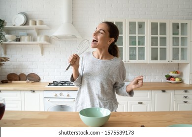 Happy young woman holding beater microphone singing song dancing cooking alone in modern kitchen, funny lady housewife having fun listening music prepare healthy morning meal doing housework at home - Powered by Shutterstock