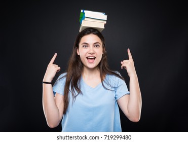 Happy young woman holding books on her head and pointing fingers to them