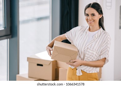 happy young woman holding box and smiling at camera during relocation 