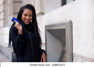 a happy young woman holding a cash card at a cash mashine.