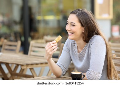 Happy Young Woman Holding A Cereal Snack Bar Sitting On A Cafe Terrace