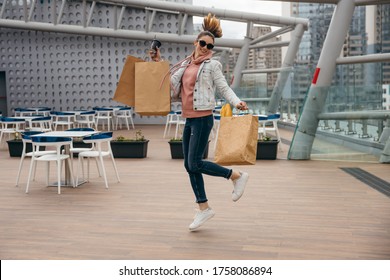 Happy Young Woman Holding Coffee Cup, Jumping With Grocery Shopping Paper Bag With Long White Bread Baguette Over City Background