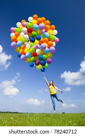 Happy young woman holding colorful balloons and flying over a green meadow