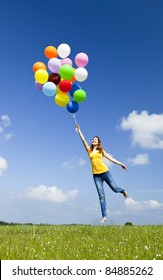 Happy young woman holding colorful balloons and flying over a green meadow