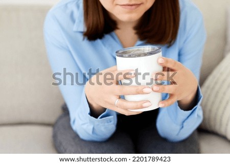 Happy young woman holding a cup in her hands. Dreaming girl sitting in living room with cup of hot coffee enjoying the rest.