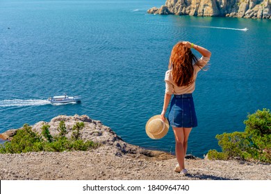 Happy Young Woman Holding A Hat And Running Down The Mountainside With A View Of The Rocks And The Sea. The Concept Of Home Away From Home