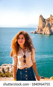 Happy Young Woman Holding A Hat And Running Down The Mountainside With A View Of The Rocks And The Sea. The Concept Of Home Away From Home