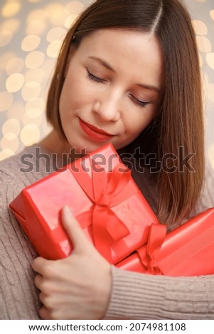 Happy young woman holding many present boxes with lights in background and copy space