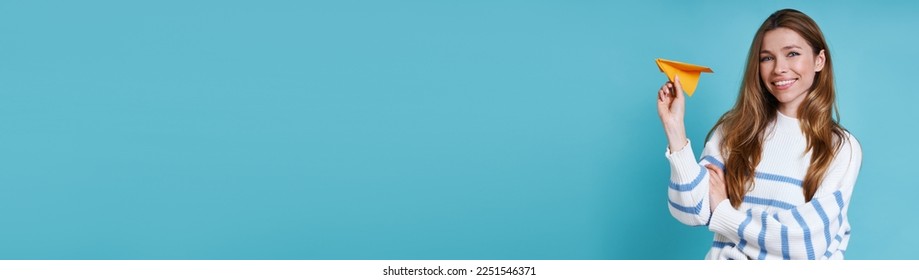 Happy young woman holding paper airplane against blue background - Shutterstock ID 2251546371