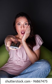 Happy young woman holding remote control and watching romantic movie by tv