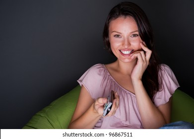 Happy young woman holding remote control and watching romantic movie by tv