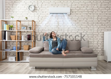 Happy Young Woman Holding Remote Control Relaxing Under The Air Conditioner