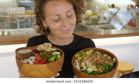 Happy Young Woman Holding And Representing Two Big Bowls Full Of Healthy Vegan Meals In Organic Cafe