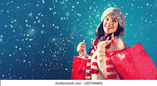 Happy young woman holding shopping bags in a snowy night - Powered by Shutterstock