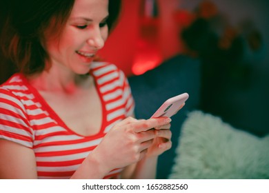 Happy Young Woman Holding Smartphone Blick auf Handy-Bildschirm lacht Freude über die Verwendung von mobilen Apps zum Einkaufen. Spaß beim Spielen im Chatting in Social Media Setzen Sie sich auf Couch zu Hause