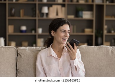 Happy Young Woman Holding Smartphone Talks On Speaker Phone Seated On Sofa At Home. Distance Communication, Leave Voice Mail Or Audio Message To Friend Use Mobile Application, Modern AI Tech Concept