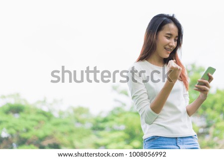 Happy young woman holding smartphone in park at outdoors.