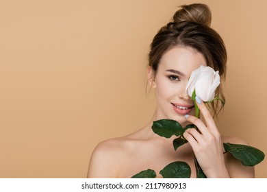 happy young woman holding white rose near face isolated on beige