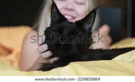 Happy young woman hugging big black Maine Coon cat in bed at home. The concept of pets and people