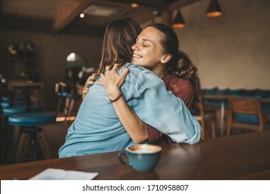 Happy young woman hugging her best friend, sitting in a cafe, having pleasant talk. - Powered by Shutterstock