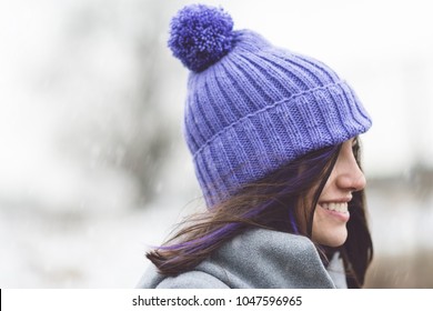 Happy Young Woman In Knitted Purple Beanie Pompom Hat, Outdoors On Snowy Winter Day. Closeup, Natural Light, No Retouch.