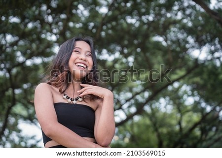 A happy young woman laughing but in a composed manner. Standing outside at a park.