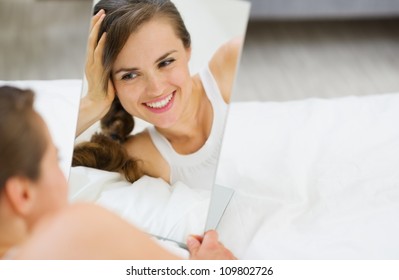 Happy Young Woman Laying On Bed And Looking On Mirror