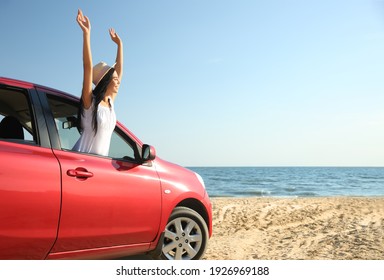Happy young woman leaning out of car window on beach, space for text. Summer trip