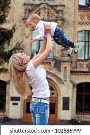 Happy Young Woman Lifting Her Son High Up Outdoors