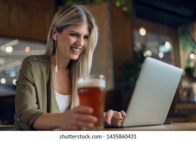 Happy young woman listening music over her laptop  in a bar