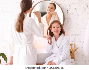 Happy young woman with little daughter in white bathrobes brushing teeth together in bathroom and enjoying morning time together - Powered by Shutterstock