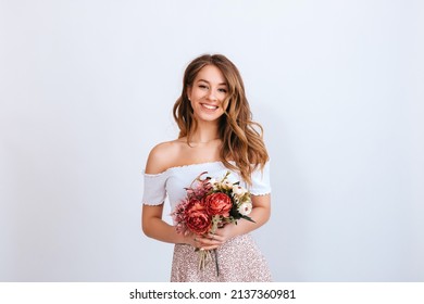 Happy young woman with long curly hair in a white dress , holds a bouquet of flowers in her hands and smiles isolated on a white background. Beautiful girl with flowers. Copy space. - Powered by Shutterstock