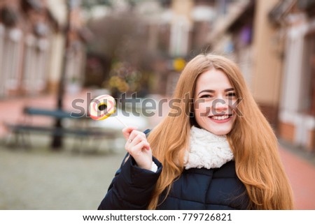 Happy young woman with long hair holding colorful lollipop at the city background