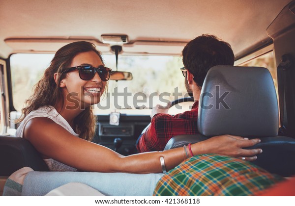 Happy young woman looking back with\
man driving car. Couple in a car going on\
roadtrip.