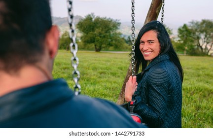 Happy Young Woman Looking Camera Sitting On A Swing In A Recreational Area